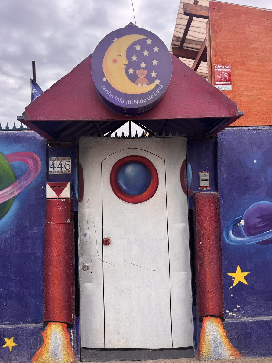 Puerta de entrada pintada como un cohete con llamas, bajo la luna y el osito del logo