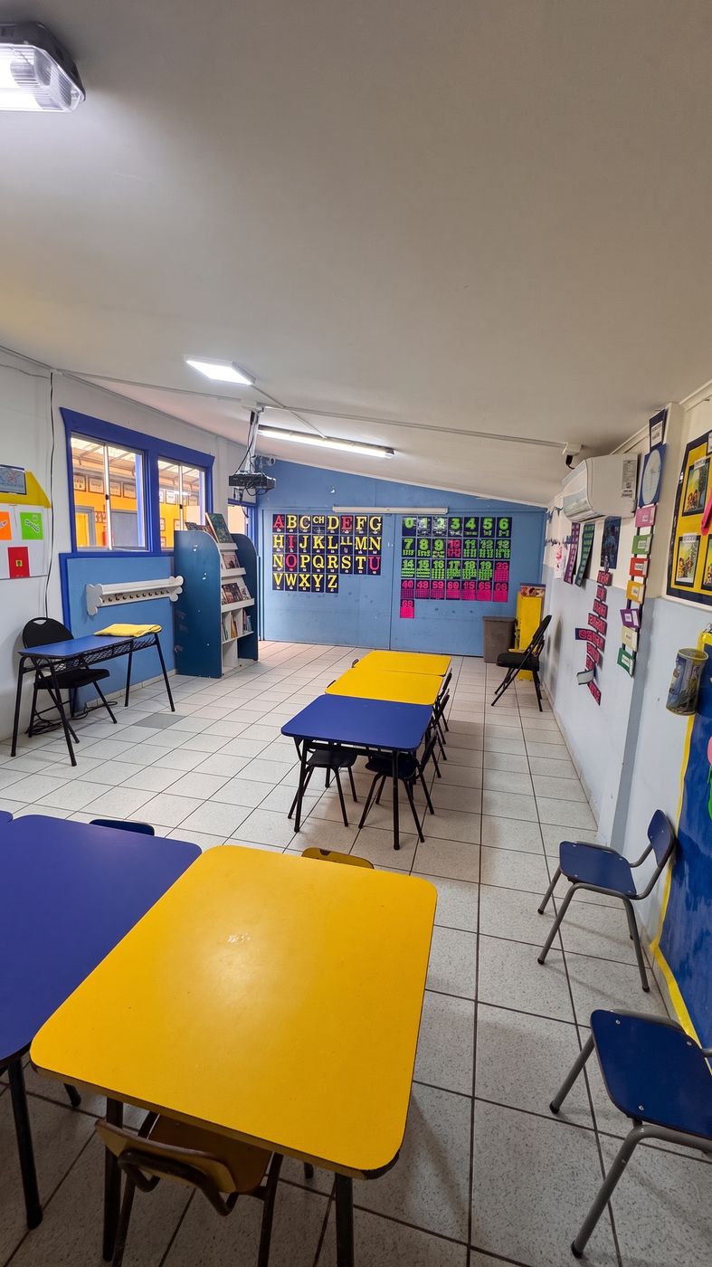 Sala de kínder, con mesas amarillas y azules y luz natural