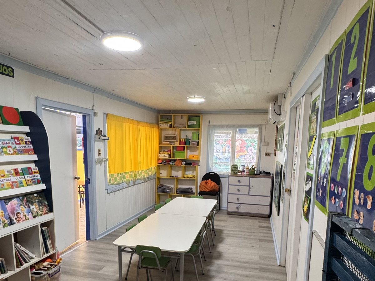 Sala de clases con piso de madera, estantería de material y cortinas amarillas